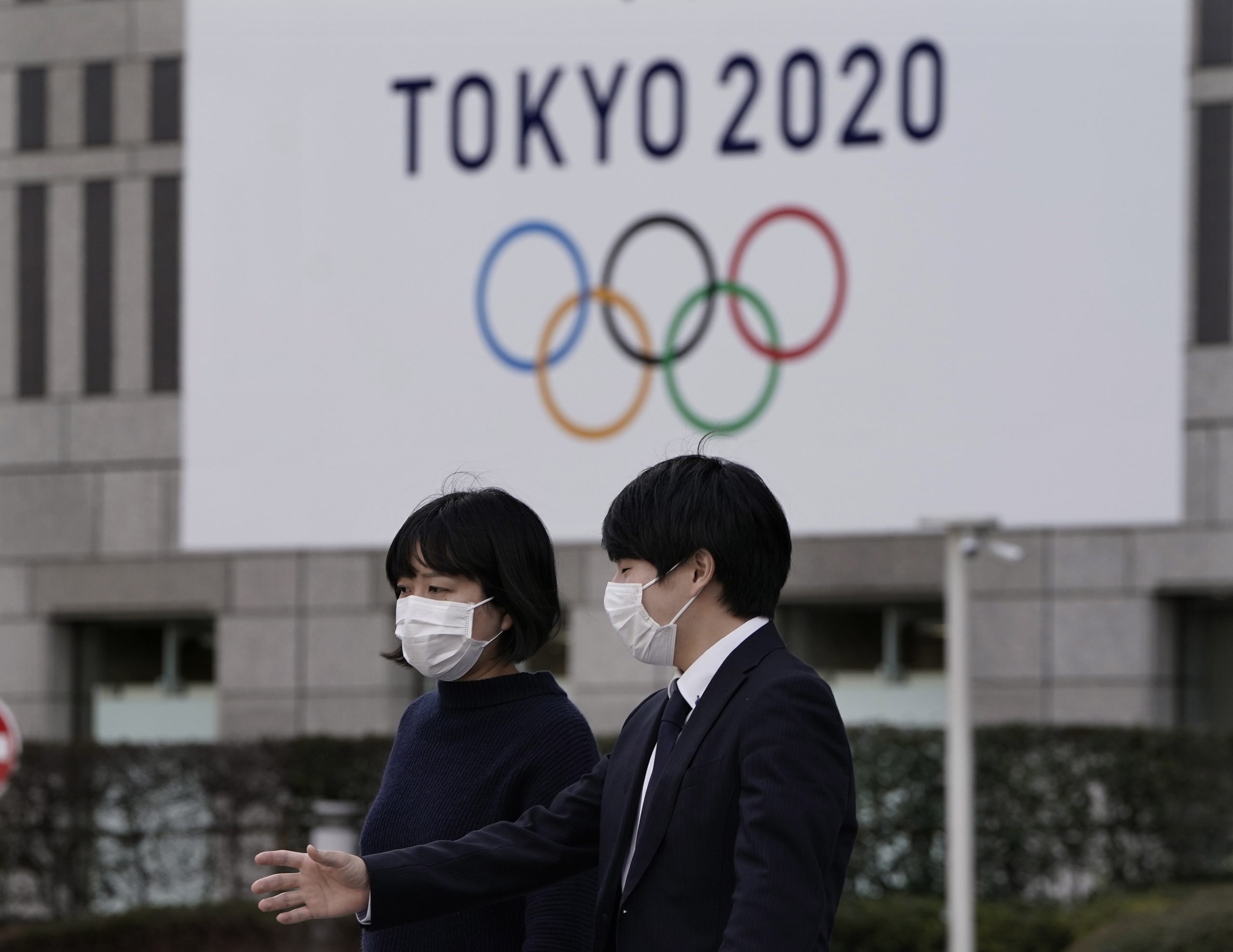 epa08314049 (FILE) - A file picture of pedestrians wearing masks walking past the emblem of the Tokyo 2020 Olympic Games displayed on a wall of Tokyo Metropolitan Government headquarters in Tokyo, Japan, 28 February 2020.  IOC informed on 22 March 2020 that they agreed for a time limit of 4 weeks to decide about the the Olympic Games Tokyo 2020. In this time frame they also want to think about options to postpone the games.  EPA/KIMIMASA MAYAMA *** Local Caption *** 55912343