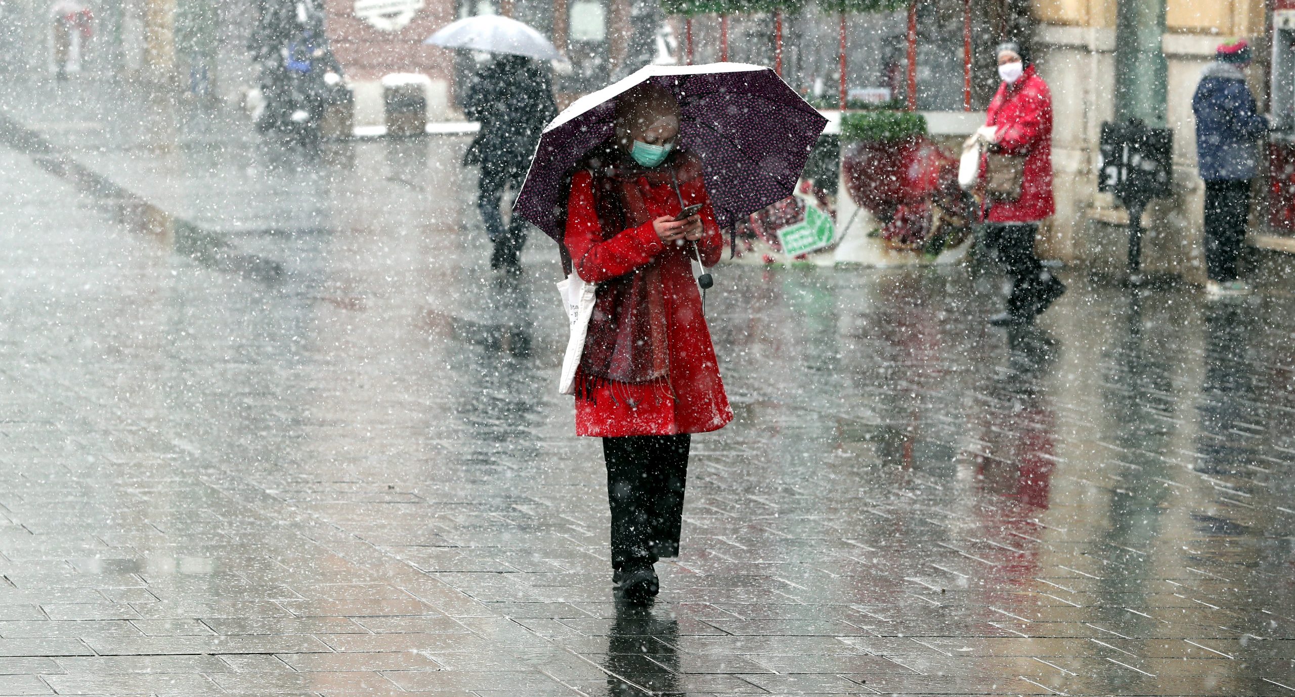 epa08334216 People wearing face masks hold up umbrellas to shield themselves from heavy snowfall in Sarajevo, Bosnia and Herzegovina, 31 March 2020. According to latest figures by WHO on 30 March, a total of 325 cases of coronavirus are confirmed in Bosnia and Herzegovina, and six deaths.  EPA/FEHIM DEMIR