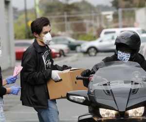 epa08351650 Members of Hope Ministries help load a box of food on a motorcycle at a drive-through food distribution provided by Second Harvest of Silicon Valley in the Boys and Girls Club parking lot in South San Francisco, California, USA, 08 April 2020. Organizations from Hope Ministries, Second Harvest, YMCA, and others are joining forces to provide food care packages ready to go for people to grab. The food distribution for drive-thru and walk-up is for families in need during the coronavirus COVID-19 outbreak.  EPA/JOHN G. MABANGLO