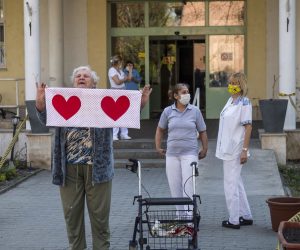 epa08351235 An older woman and personnel show their appreciation as they listen to classical music being transmitted from a car of the MAV Symphonic Orchestra outside the Olive Branch nursing home for elder people in the Csepel neighborhood of Budapest, Hungary, 08 April 2020, during the COVID-19 pandemic caused by the SARS-CoV-2 coronavirus.  EPA/Marton Monus HUNGARY OUT