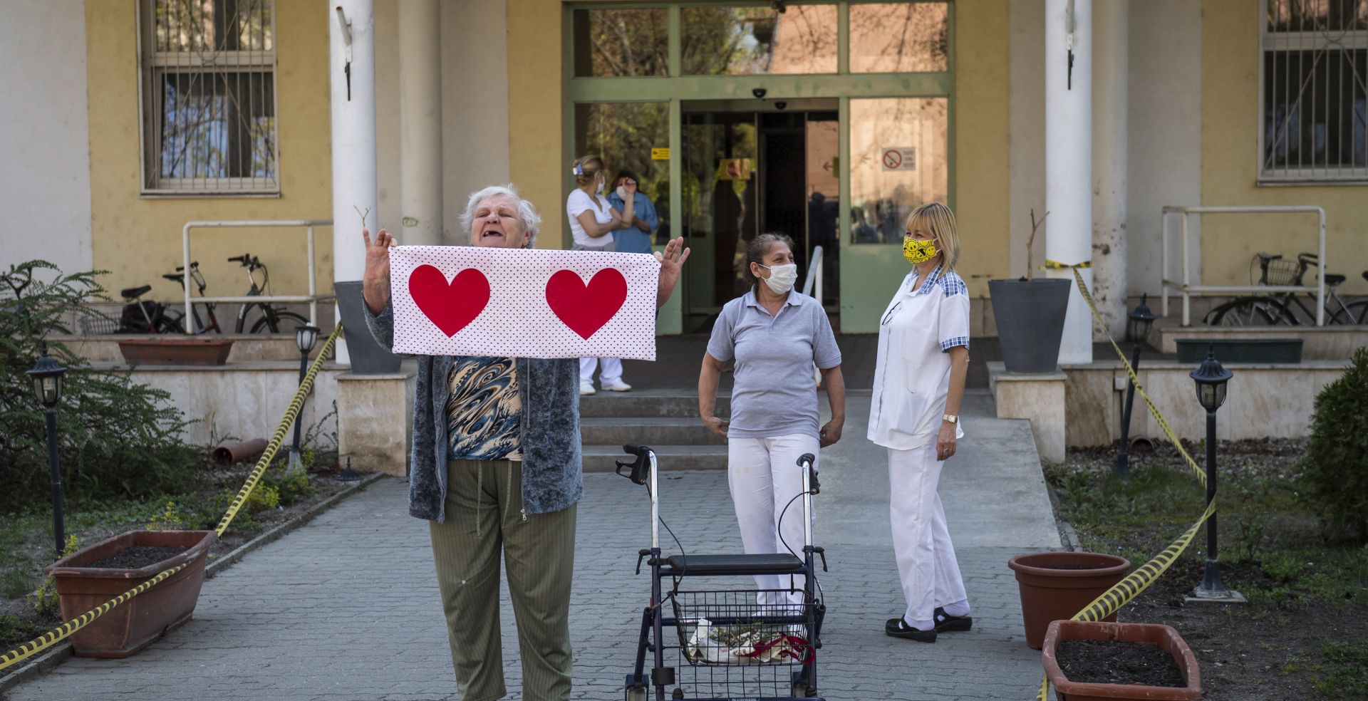 epa08351235 An older woman and personnel show their appreciation as they listen to classical music being transmitted from a car of the MAV Symphonic Orchestra outside the Olive Branch nursing home for elder people in the Csepel neighborhood of Budapest, Hungary, 08 April 2020, during the COVID-19 pandemic caused by the SARS-CoV-2 coronavirus.  EPA/Marton Monus HUNGARY OUT