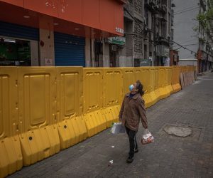 epa08354679 A woman wearing a protective face mask walks next to a security fence separating a residential area from a street, in Wuhan, China, 10 April 2020. Wuhan, the epicenter of the coronavirus outbreak, lifted the lockdown on 08 April 2020, allowing people to leave the city after more than two months.  EPA/ROMAN PILIPEY