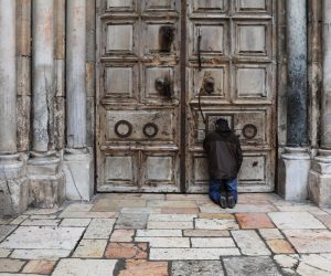 epa08355363 People pray at the closed doors of the Church of the Holy Sepulcher during the Good Friday procession in the Old City of Jerusalem, 10 April 2020. Media reports state, that according to government decision, Israeli police have enforced lockdown on several cities and ultra-Orthodox Jewish neighborhoods across the country  in order to prevent the spread of the SARS-CoV-2 coronavirus which causes the Covid-19 disease during the holidays season.  EPA/ABIR SULTAN
