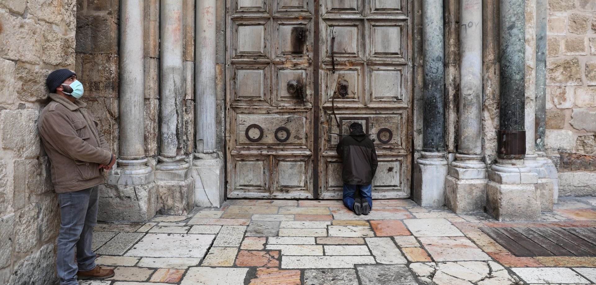 epa08355363 People pray at the closed doors of the Church of the Holy Sepulcher during the Good Friday procession in the Old City of Jerusalem, 10 April 2020. Media reports state, that according to government decision, Israeli police have enforced lockdown on several cities and ultra-Orthodox Jewish neighborhoods across the country  in order to prevent the spread of the SARS-CoV-2 coronavirus which causes the Covid-19 disease during the holidays season.  EPA/ABIR SULTAN