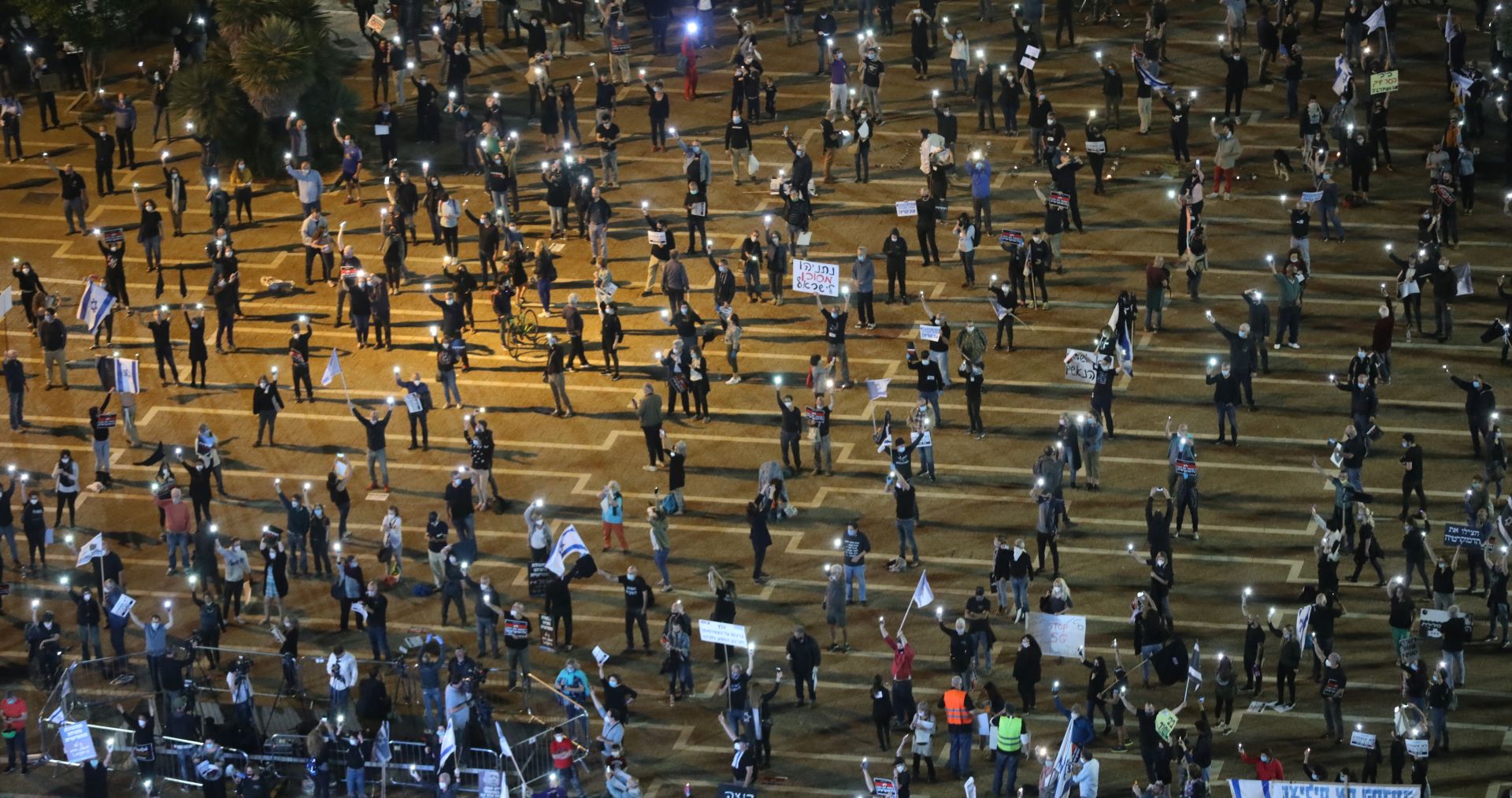 epa08372029 Israelis turn on their mobile phone lights as they protest against government corruption and for democracy at Rabin square in Tel Aviv, Israel, 15 April 2020. Reports state that around 2,000 people took part in the demonstration keeping two meters distance from each other in order to prevent the spread of the SARS-CoV-2 coronavirus which causes he Covid-19 disease.  EPA/ABIR SULTAN