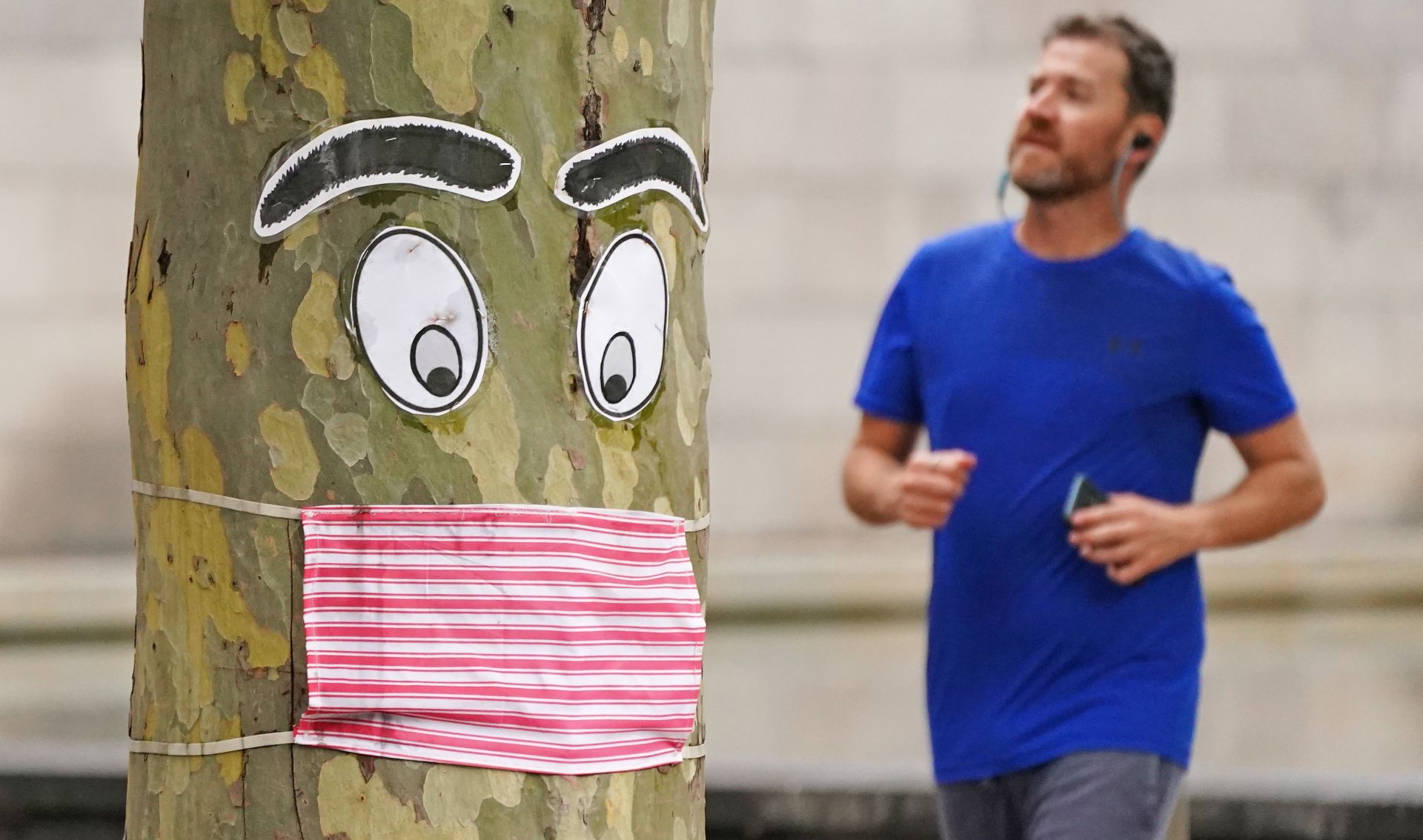 epaselect epa08384674 A man runs past a tree with a face mask and eyes stapled to it in Melbourne, Australia, 26 April 2020. Authorities have said social distancing and isolation measures could still remain in place for the next six months.  A shutdown of non-essential services is in effect Australia wide in a bid to slow the spread of the coronavirus (COVID-19) disease.  EPA/SCOTT BARBOUR NO ARCHIVING AUSTRALIA AND NEW ZEALAND OUT
