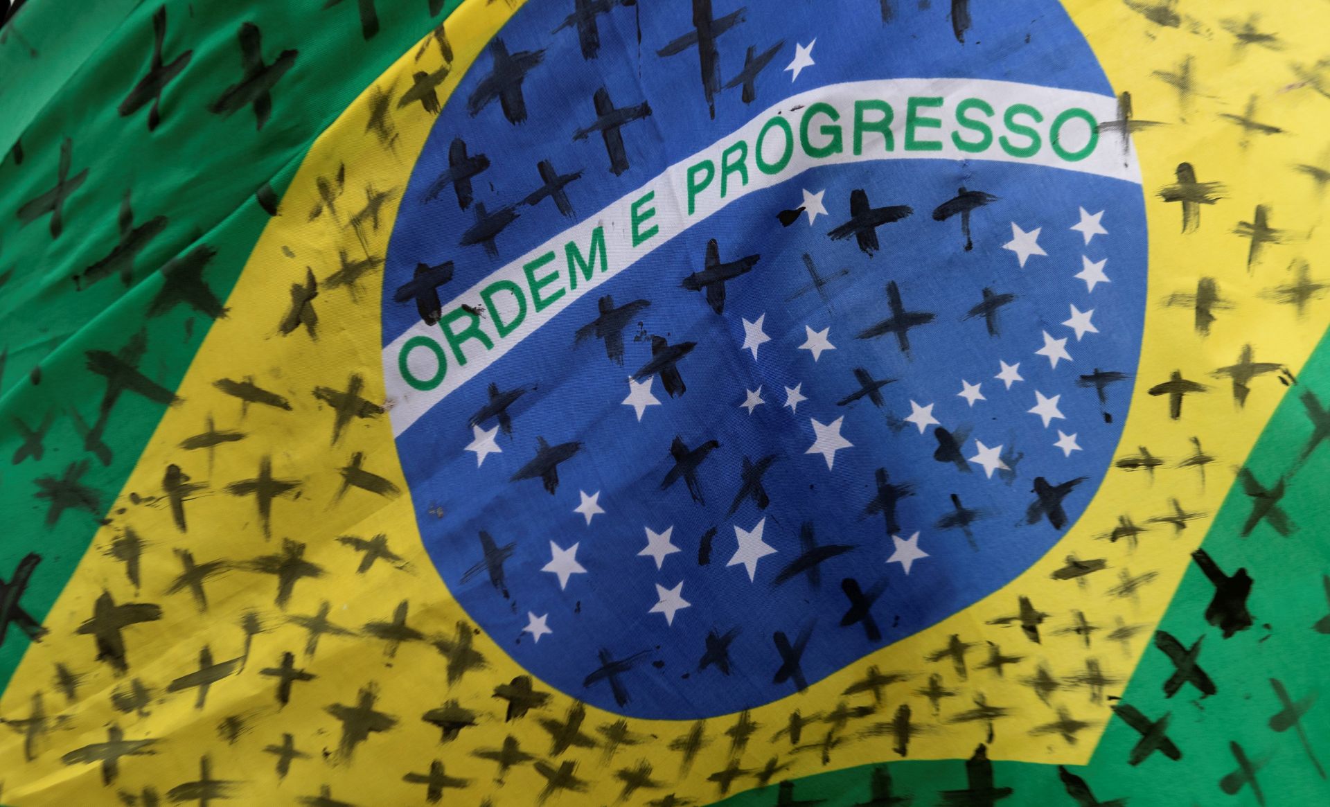 epa08434295 Detail of a Brazilian flag with black crosses painted to honor and remember the victims of covid-19 in that country, during a protest against the President of Brazil, Jair Bolsonaro, at the Planalto Palace in Brasilia, Brazil, 20 May 2020. Convened by the members of the popular committee 'Bolsonaro Out', dozens of people participated in the demonstration that rejected Bolsonaro's statements and actions during the handling of the coronavirus crisis, which left more than 17,000 deaths in the South American country.  EPA/JOEDSON ALVES