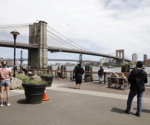 epa08438271 People on the street watch as New York City Police officers talk to a man who climbed atop the Brooklyn Bridge in Brooklyn, New York, USA, 22 May 2020.  EPA/Jason Szenes