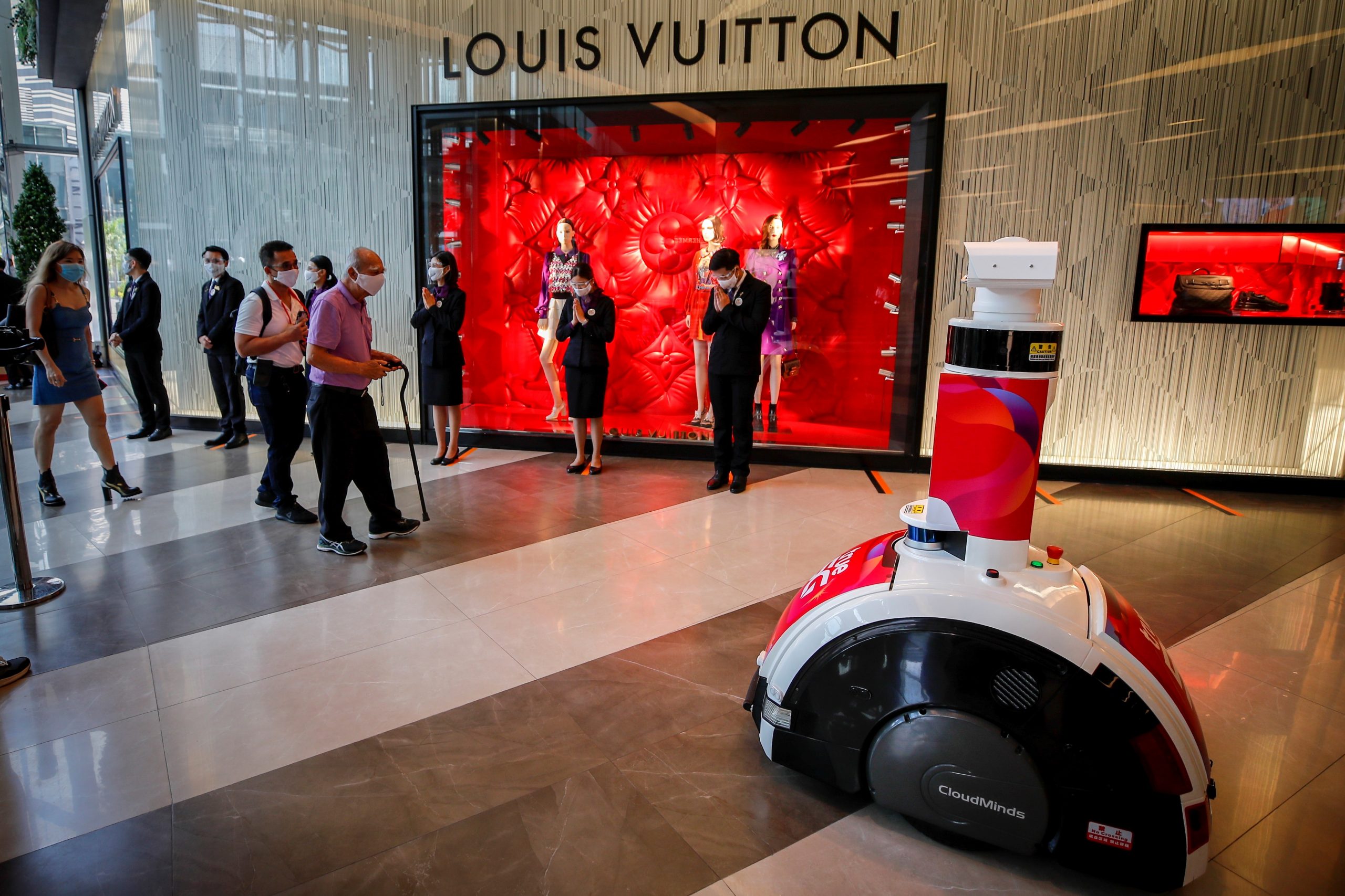 epa08427336 People wearing protective masks walk past a smart robot used for screening and body temperature as they enter a shopping mall on the first day of reopening in Bangkok, Thailand, 17 May 2020. Thailand has allowed shopping malls to reopen nationwide while observing social distancing, after they were closed on 22 March as part of coronavirus restrictions in a bid to stem the spread of the SARS-CoV-2 coronavirus which causes the COVID-19 disease.  EPA/DIEGO AZUBEL