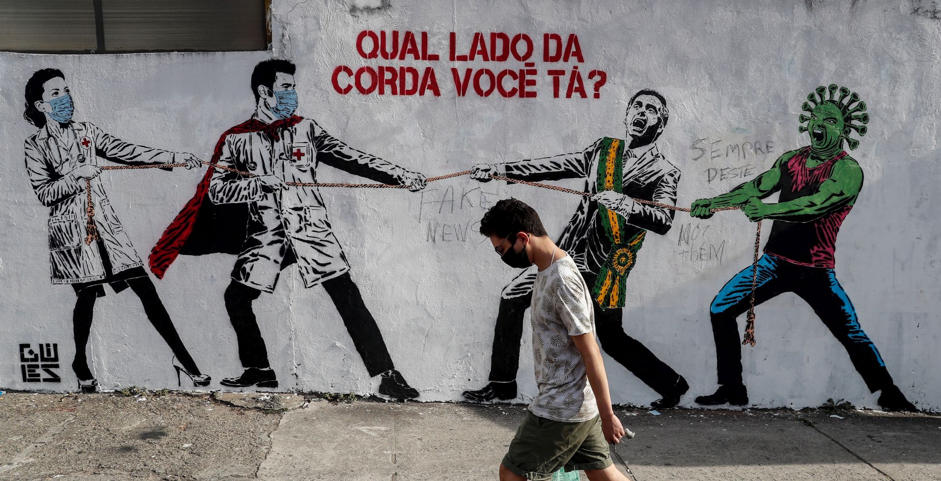 epa08504708 A man passes in front of a graffiti that represents Brazilian President Jair Bolsonaro and a figure that represents the novel coronavirus COVID-19 pulling a rope against health workers with a message that says: 'Which side of the rope are you on?' in Sao Paulo, Brazil, 23 June 2020.  EPA/Sebastiao Moreira