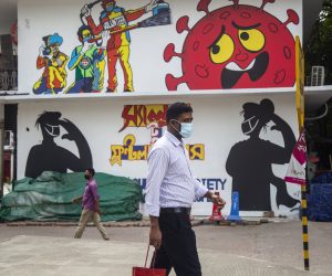epa08513536 Bangladeshi people wearing face masks walk in front of graffiti in Dhaka, Bangladesh, 28 June 2020. Countries around the world are taking increased measures to stem the spread of the SARS-CoV-2 coronavirus which causes the COVID-19 disease.  EPA/MONIRUL ALAM