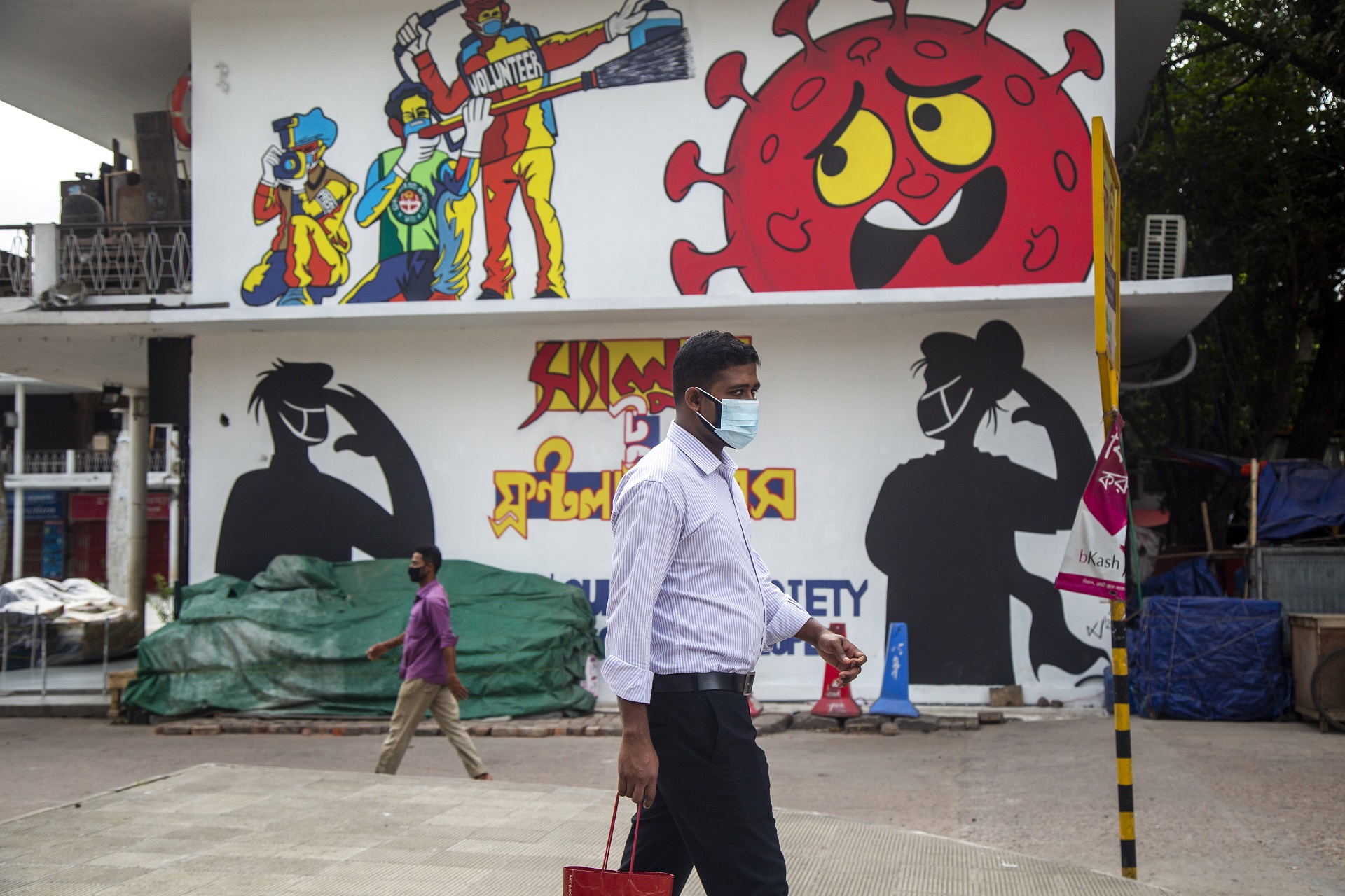 epa08513536 Bangladeshi people wearing face masks walk in front of graffiti in Dhaka, Bangladesh, 28 June 2020. Countries around the world are taking increased measures to stem the spread of the SARS-CoV-2 coronavirus which causes the COVID-19 disease.  EPA/MONIRUL ALAM