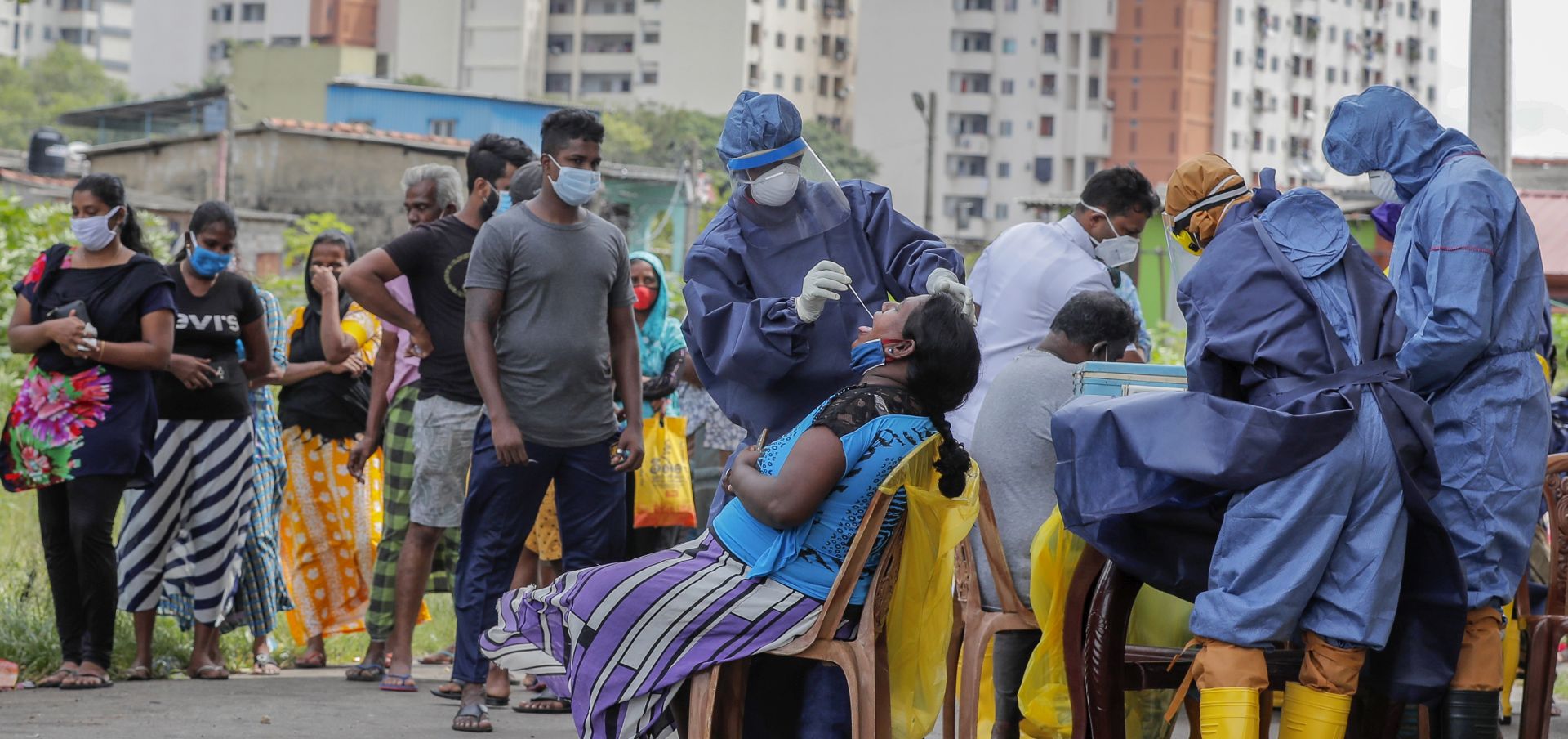 epa08546927 Sri Lankan health workers wearing protective equipment perform coronavirus disease (COVID-19) tests as peoples wait in a queue in Colombo, Sri Lanka, 15 July 2020. The Sri Lankan government has lifted most of the coronavirus restrictions, which were implemented nearly four months ago, and is preparing for a full reopening of businesses and activities to avoid an economic slump.  EPA/CHAMILA KARUNARATHNE