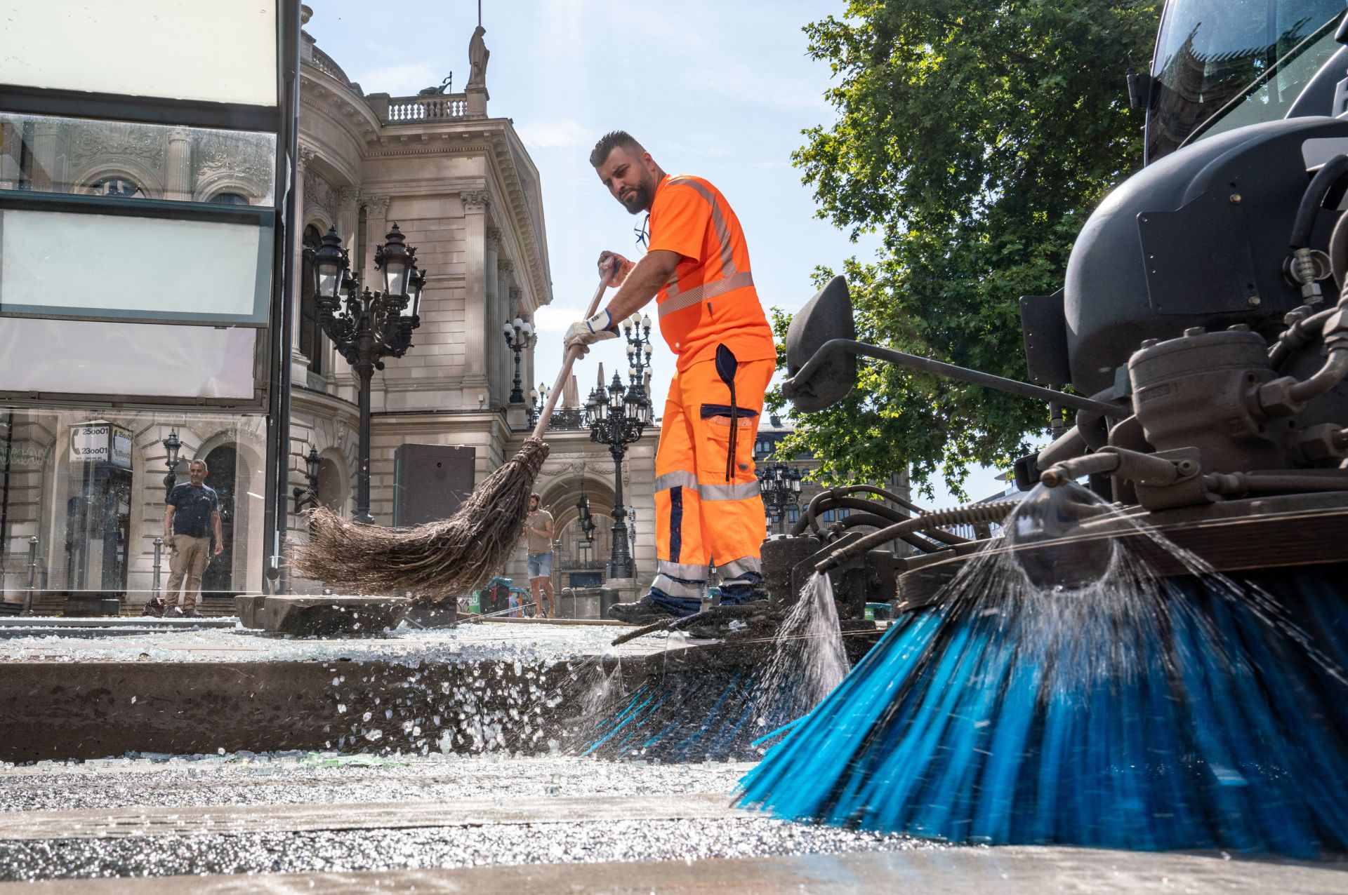 19 July 2020, Hessen, Frankfurt/Main: A member of the city cleaning service removes shards of broken glass from a bus stop in front of the Alte Oper. Nearly 40 people were arrested in the heart of Frankfurt after violent rioting broke out during a massive outdoor party near the German city's concert hall, police said on Sunday. Photo: Frank Rumpenhorst/dpa