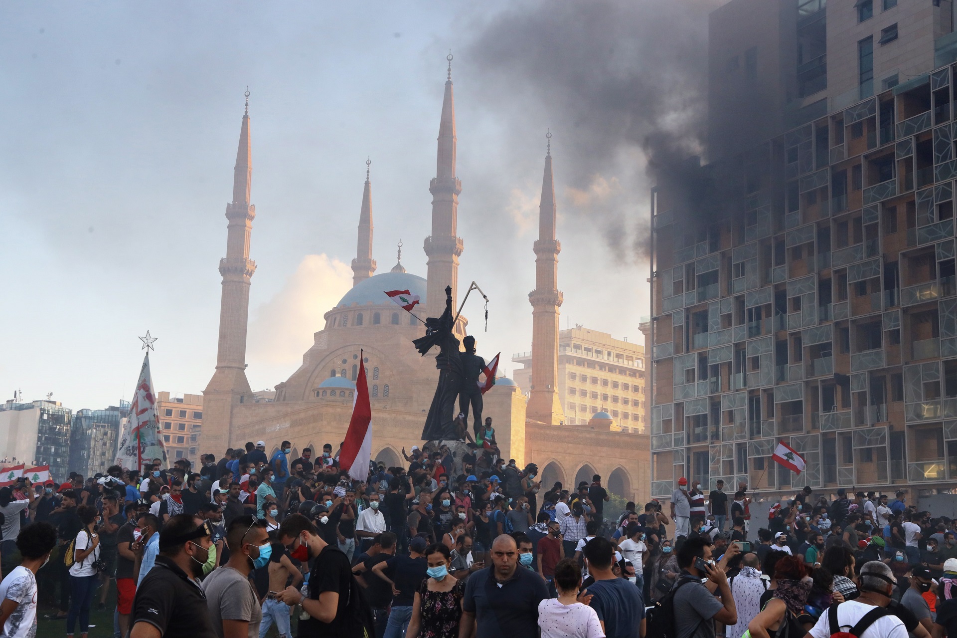 epa08592272 Smoke rises from the Beirut Gardens building as Lebanese people gather at Martyr's Square during a protest in the aftermath of the port explosion, in Beirut, Lebanon, 08 August 2020. People gathered for the so-called 'the Saturday of the hanging ropes' to protest against the political leaders and calling on those responsible over the explosion to be held accountable. Lebanese Health Ministry on 07 August said at least 154 people were killed, and more than 5,000 injured in the Beirut blast that devastated the port area on 04 August and believed to have been caused by an estimated 2,750 tons of ammonium nitrate stored in a warehouse.  EPA/IBRAHIM DIRANI DAR AL MUSSAWIR