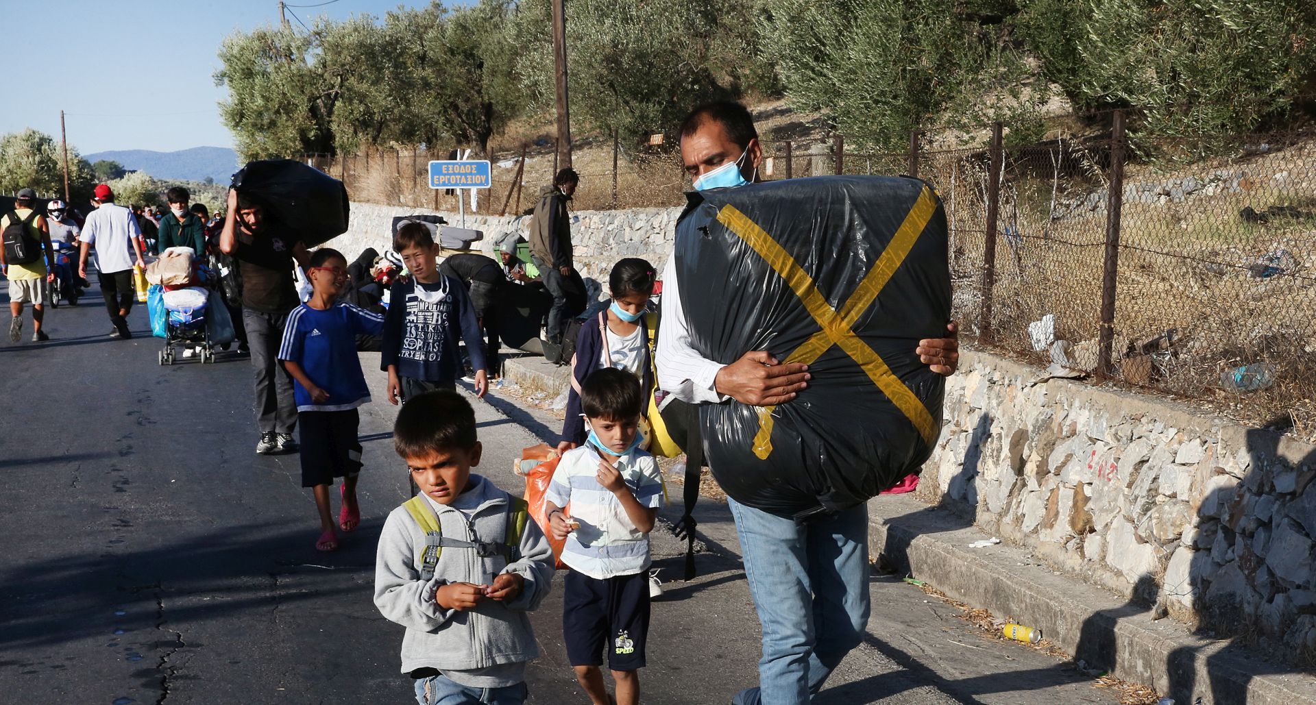 epa08658104 Asylum seekers evacuate from Moria refugee camp after a fire that broke out in the camp, Greece, 10 September 2020. A passenger ferry and two Navy landing ships will accommodate about 2,000 refugees who are homeless after the fire at Moria, Migration and Asylum Minister Notis Mitarachi said. The island of Lesvos was declared in state of emergency for four months, by order of Deputy Civil Protection and Management Crises Minister Nikos Hardalias and the general secretary of civil protection Vassilis Papageorgiou.  EPA/ORESTIS PANAGIOTOU