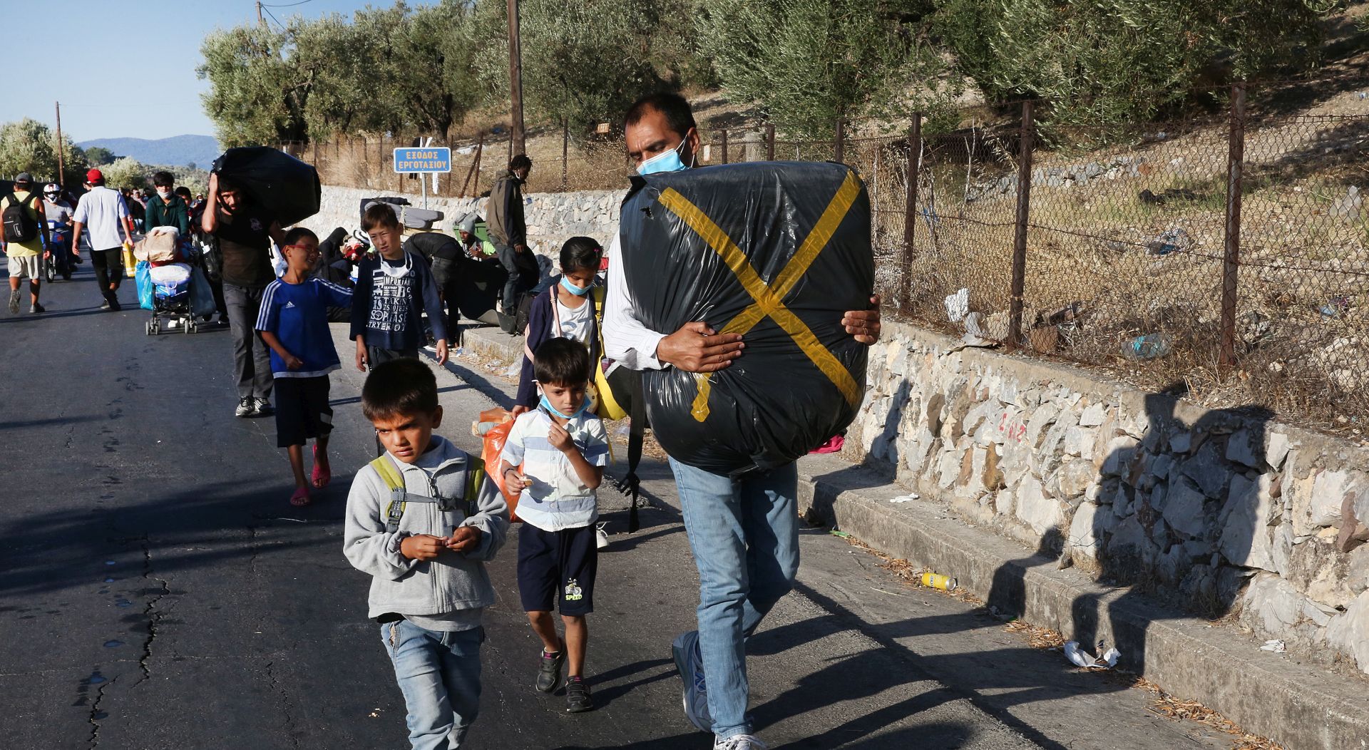 epa08658104 Asylum seekers evacuate from Moria refugee camp after a fire that broke out in the camp, Greece, 10 September 2020. A passenger ferry and two Navy landing ships will accommodate about 2,000 refugees who are homeless after the fire at Moria, Migration and Asylum Minister Notis Mitarachi said. The island of Lesvos was declared in state of emergency for four months, by order of Deputy Civil Protection and Management Crises Minister Nikos Hardalias and the general secretary of civil protection Vassilis Papageorgiou.  EPA/ORESTIS PANAGIOTOU