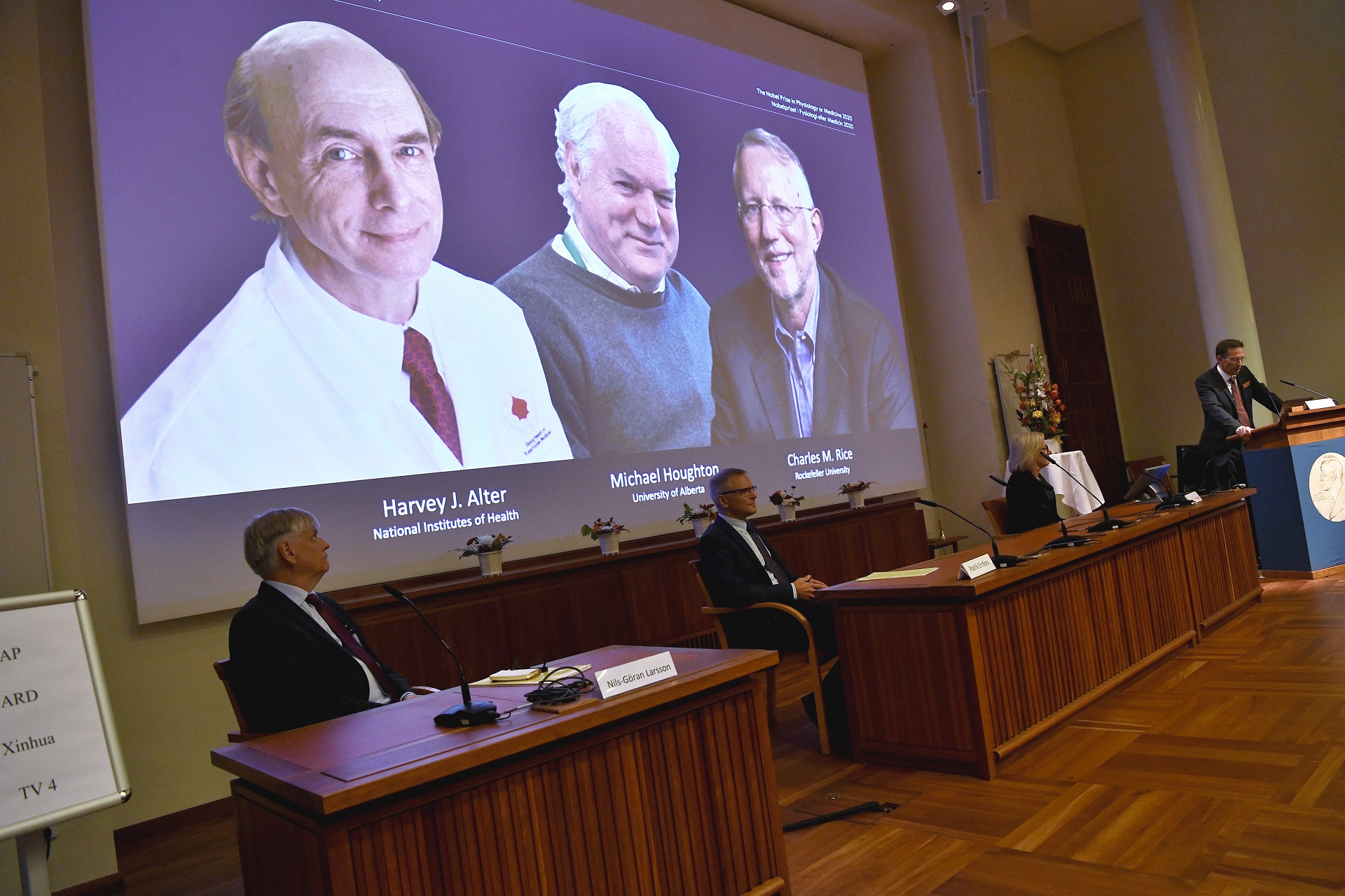 epa08721714 Thomas Perlmann (R), Secretary of the Nobel Assembly at the Karolinska Institut and of the Nobel Committee for Physiology or Medicine, announces the winners of the 2020 Nobel Prize in Physiology or Medicine during a press conference at the Karolinska Institute in Stockholm, Sweden, 05 October 2020. (L-R) on the screen are Harvey J.  Alter, Michael Houghton and Charles M  Rice, the three laureates who win the 2020 Nobel Medicine Prize.  EPA/Claudio Bresciani / POOL SWEDEN OUT