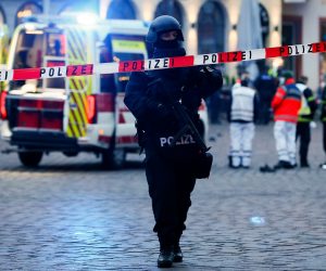 epa08855062 An armed policeman stands behind warning tape in a pedestrian zone in the city center in Trier, Germany, 01 December 2020. According to reports, at least two people have been killed and several injured after a car with high speed hit into pedestrians in the inner city of Trier. Police arrested the  driver and the car was seized.  EPA/JULIEN WARNAND