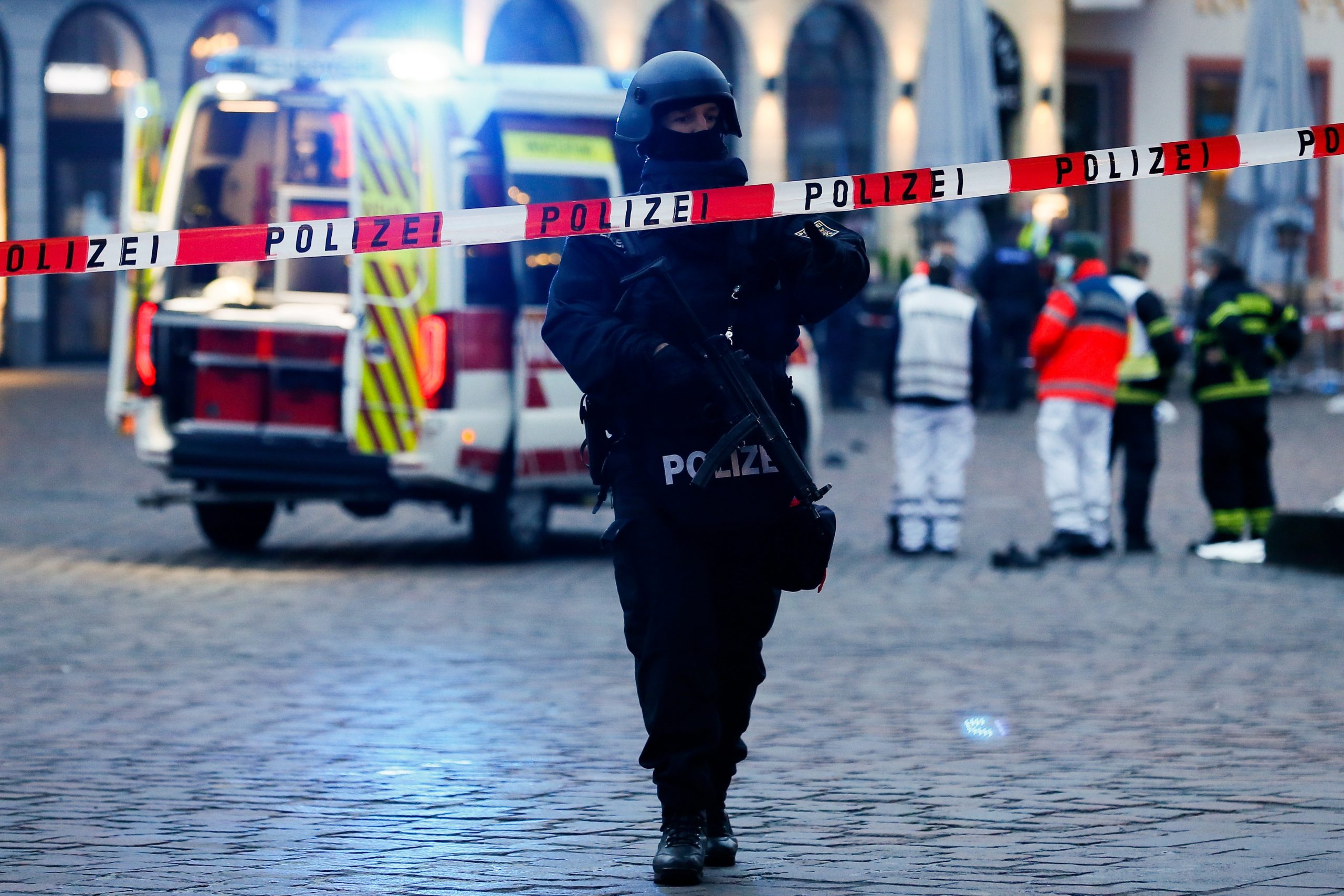 epa08855062 An armed policeman stands behind warning tape in a pedestrian zone in the city center in Trier, Germany, 01 December 2020. According to reports, at least two people have been killed and several injured after a car with high speed hit into pedestrians in the inner city of Trier. Police arrested the  driver and the car was seized.  EPA/JULIEN WARNAND