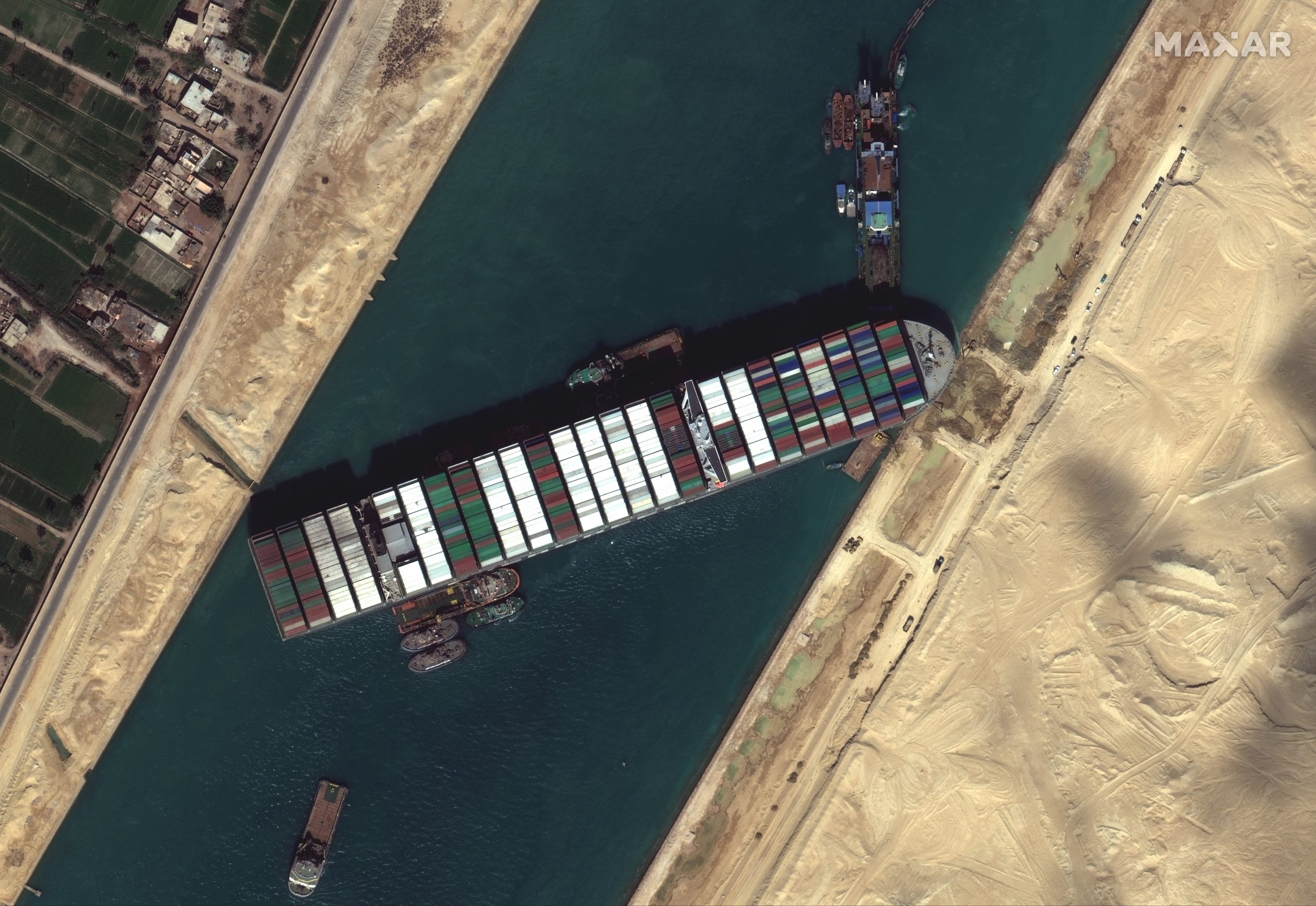 epa09101181 A handout satellite image made available by MAXAR Technologies shows multiple tug boats positioned alongside the 'Ever Given' and dredging operations in progress, in the Suez Canal, Egypt, 27 March 2021. The large container ship Ever Given ran aground in the Suez Canal on 23 March, blocking passage of other ships and causing a traffic jam for cargo vessels. The head of the Suez Canal Authority announced on 25 March that 'the navigation through the Suez Canal is temporarily suspended' until the floatation of the Ever Given is completed. Its floatation is being carried out by eight large tugboats that are towing and pushing the grounding vessel.  EPA/MAXAR TECHNOLOGIES HANDOUT -- MANDATORY CREDIT: SATELLITE IMAGE 2020 MAXAR TECHNOLOGIES -- the watermark may not be removed/cropped -- HANDOUT EDITORIAL USE ONLY/NO SALES HANDOUT EDITORIAL USE ONLY/NO SALES