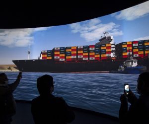 epa09104782 Reporters stand in front of a screen displaying a simulation of the pulling of Ever Given container ship in the Suez Canal, demonstrated during a press conference at the Maritime Training and Simulation Centre of the Suez Canal Authority in Ismailia, Egypt, 29 March 2021. The Suez Canal Authority announced on 29 March that the large container ship, which ran aground in the Suez Canal on 23 March, was partly refloated after responding to the pulling maneuvers and the back of the ship is now 102 meters away from the bank of the canal.  EPA/Mohamed Hossam