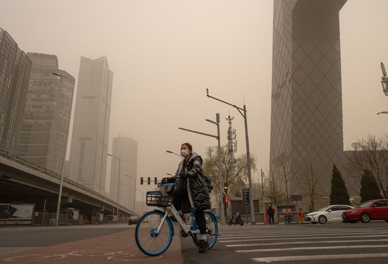 epa09102495 A woman wearing a protective face mask waits on a bicycle in the Central Business District (CBD) area amid a sandstorm in Beijing, China, 28 March 2021. A new sandstorm hit Beijing on 28 March as the city was already in the grip of high air pollution levels.  EPA/ROMAN PILIPEY