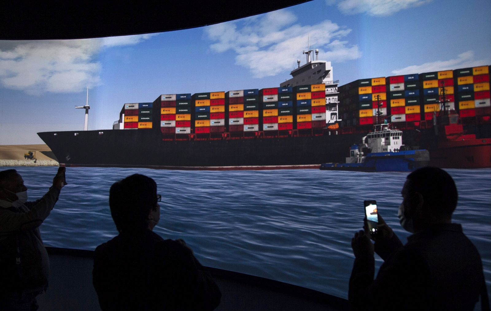 epa09104782 Reporters stand in front of a screen displaying a simulation of the pulling of Ever Given container ship in the Suez Canal, demonstrated during a press conference at the Maritime Training and Simulation Centre of the Suez Canal Authority in Ismailia, Egypt, 29 March 2021. The Suez Canal Authority announced on 29 March that the large container ship, which ran aground in the Suez Canal on 23 March, was partly refloated after responding to the pulling maneuvers and the back of the ship is now 102 meters away from the bank of the canal.  EPA/Mohamed Hossam
