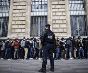 epa09193884 A riot police officer stands guard as several hundred migrants line up along a building, awaiting registration and transportation by NGO's to take them to stable accommodation, on Place de la Republique in central Paris, France, 12 May 2021. Several hundred homeless migrants gather in central Paris' Republique square to seek decent and stable housing.  EPA/IAN LANGSDON