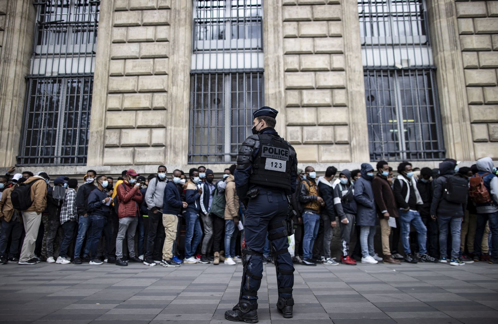 epa09193884 A riot police officer stands guard as several hundred migrants line up along a building, awaiting registration and transportation by NGO's to take them to stable accommodation, on Place de la Republique in central Paris, France, 12 May 2021. Several hundred homeless migrants gather in central Paris' Republique square to seek decent and stable housing.  EPA/IAN LANGSDON