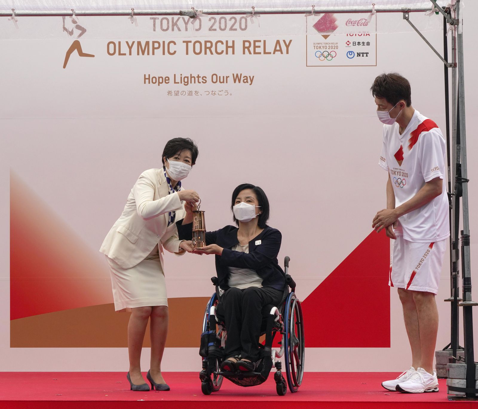 epa09332732 Aki Taguchi (C), official Ambassador of the Tokyo 2020 Torch Relay and Paralympian, hands over the Olympic Flame on a lantern to Tokyo Governor Yuriko Koike (L) during the unveiling ceremony for the Olympic Flame of the Tokyo 2020 Olympic Torch Relay at the Komazawa Olympic Park General Sports Ground in Tokyo, Japan, 09 July 2021. The Tokyo 2020 Olympic Torch Relay finally arrived in Tokyo on 09 July, two weeks before the opening of the Tokyo 2020 Olympic Games, which was delayed for one year due to the COVID-19 and Coronavirus pandemic. A five-party meeting decided on 08 July 2021 Tokyo venues for the Summer Games will be held without spectators.  EPA/KIMIMASA MAYAMA