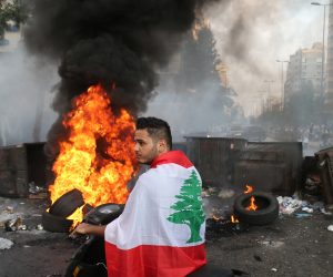 epaselect epa09347091 A Lebanese man drives as protesters block the roads with garbage bins and burning tires during protests after Lebanese Prime Minister-Designate Saad Hariri abandoned his effort to form a new government, in Beirut, Lebanon, 15 July 2021. Hariri, who was tasked nine months ago with forming the new government, said on 15 July he is stepping down a day after he presented the cabinet proposal to President Michel Aoun who has not accepted the government.  EPA/NABIL MOUNZER