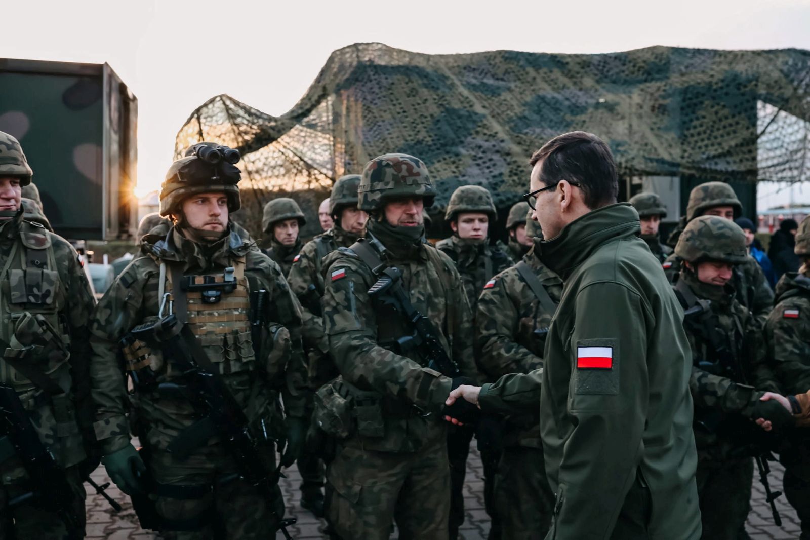 epa09572684 A handout photo made available by Chancellery of the Prime Minister shows 
Polish Prime Minister Mateusz Morawiecki (R), during a meeting with soldiers and officers of the services involved in securing the Polish border with Belarus in the region of Kuznica, eastern-Poland, 09 November 2021. On 08 November morning, the media published information about a large group of migrants planning to cross the Belarusian border with Poland. The Ministry of National Defense informed in the afternoon that the services of the Ministry of Interior and Administration and soldiers had managed to stop the first mass attempt to cross the border. Currently, migrants have set up a camp in the Kuznica region.  EPA/ADAM GUZ / CHANCELLERY OF PRIME MINISTER HANDOUT  HANDOUT EDITORIAL USE ONLY/NO SALES