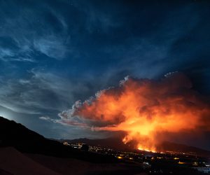 epa09592807 Lava and smoke rise from the Cumbre Vieja volcano as it is seen from Los Llanos de Aridane, La Palma, Canary Islands, Spain, 19 November 2021. The Cumbre Vieja volcano erupted on 19 September and has spewn out smoke, ash and lava since then.  EPA/Miguel Calero