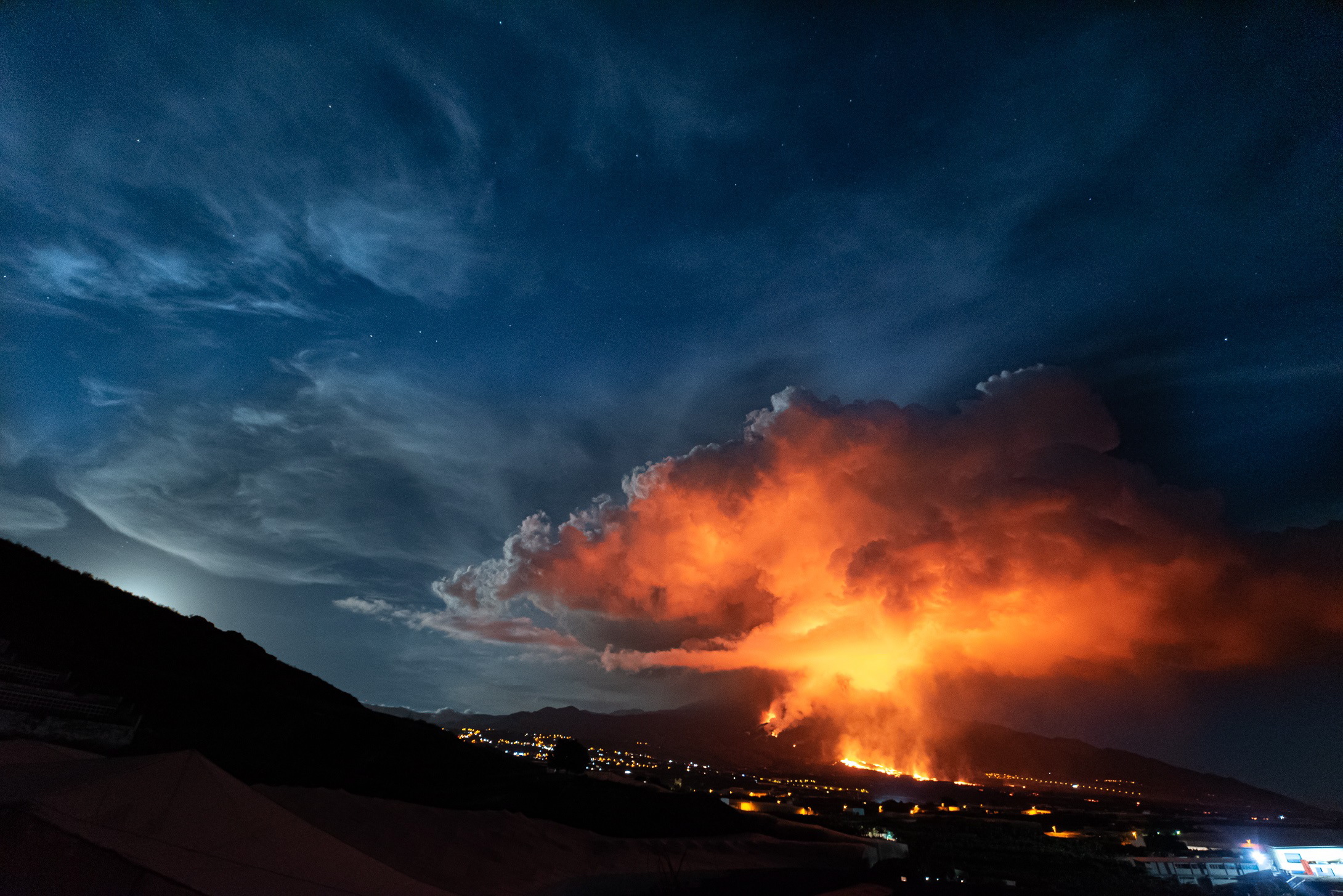 epa09592807 Lava and smoke rise from the Cumbre Vieja volcano as it is seen from Los Llanos de Aridane, La Palma, Canary Islands, Spain, 19 November 2021. The Cumbre Vieja volcano erupted on 19 September and has spewn out smoke, ash and lava since then.  EPA/Miguel Calero