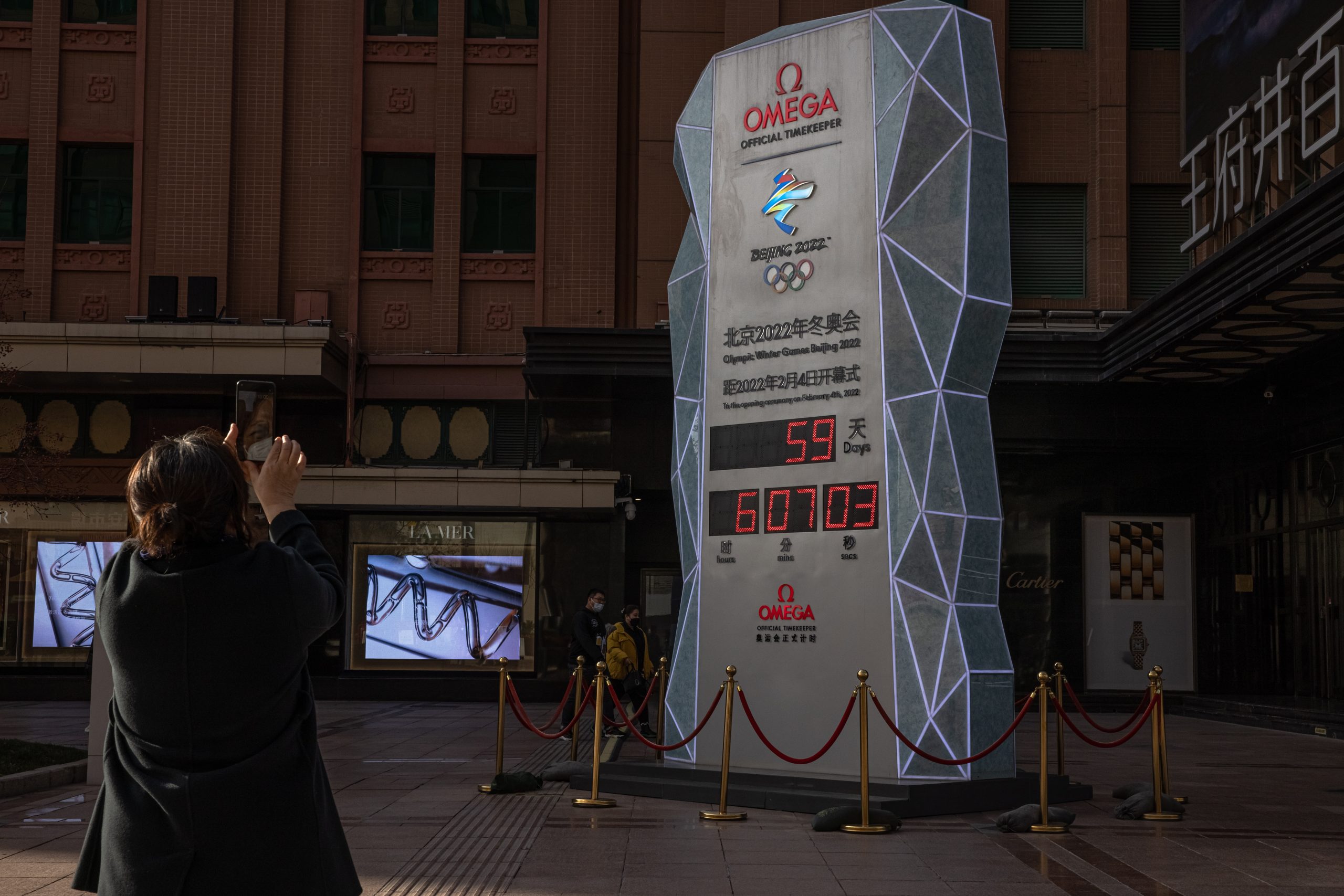 epa09626624 A woman stands in front of a countdown display showing days left for the Beijing 2022 Winter Olympics, on a shopping street in Beijing, China, 07 December 2021. US officials announced a diplomatic boycott of the 2022 Beijing Winter Olympics as a result of as it described ongoing genocide and crimes against humanity in Xinjiang and other human rights abuses in China. US athletes would still be taking part in the Games. The 2022 Beijing Winter Olympics is scheduled to begin in less than two months.  EPA/ROMAN PILIPEY
