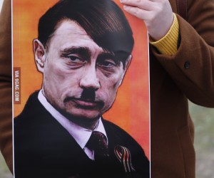 epa09780337 A person holds a placard showing Vladimir Putin dressed as Adolf Hitler as people protest against Russia's military operation in Ukraine, outside the Russian Embassy in Riga, Latvia, 24 February 2022. Russian troops entered Ukraine on 24 February. Country's President Volodymyr Zelensky addressed the nation to announce the imposition of martial law.  EPA/TOMS KALNINS