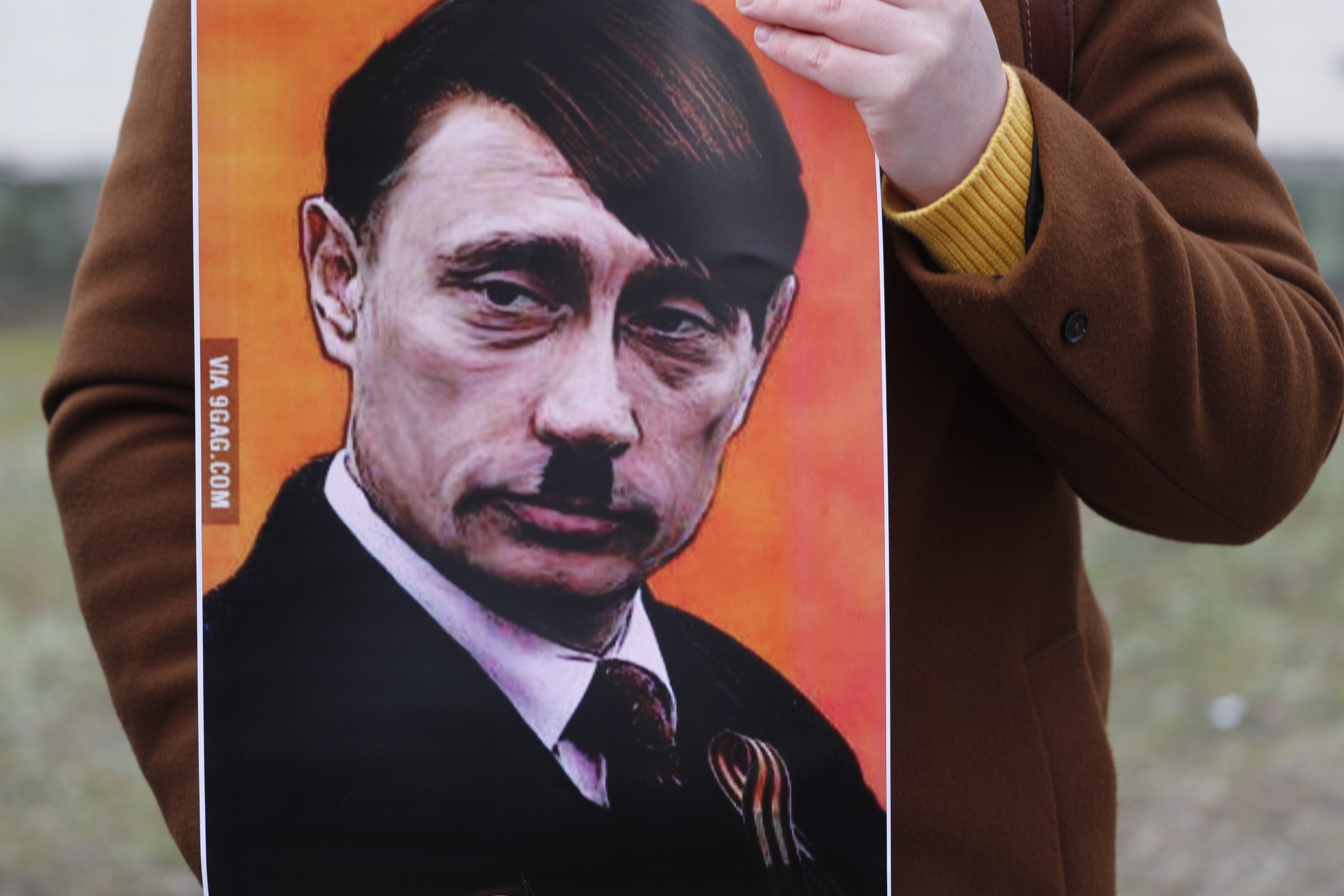 epa09780337 A person holds a placard showing Vladimir Putin dressed as Adolf Hitler as people protest against Russia's military operation in Ukraine, outside the Russian Embassy in Riga, Latvia, 24 February 2022. Russian troops entered Ukraine on 24 February. Country's President Volodymyr Zelensky addressed the nation to announce the imposition of martial law.  EPA/TOMS KALNINS