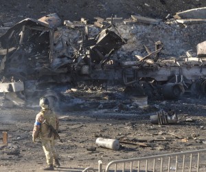 epa09786493 A Ukrainian serviceman stands near a charred vehicle after night fighting in Kiev, Ukraine, 26 February 2022. Russian troops entered Ukraine on 24 February prompting the country's president to declare martial law and triggering a series of announcements by Western countries to impose severe economic sanctions on Russia.  EPA/ANDRII NESTERENKO