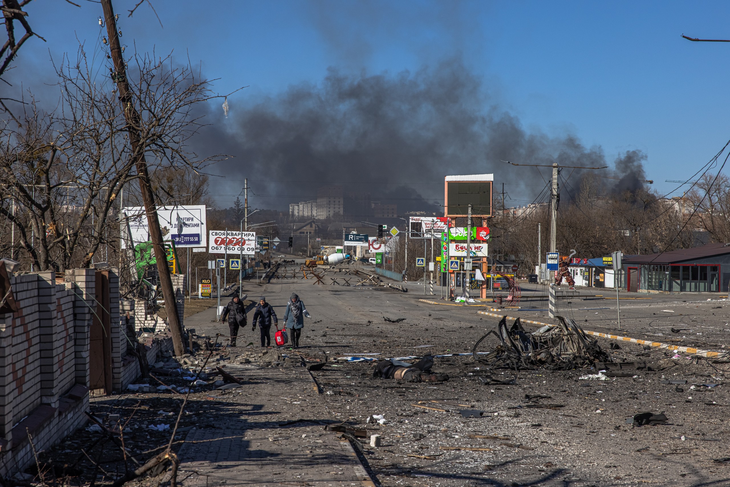 epa09814869 Residents coming from Bucha town, which is currently controlled by the Russian military, walk with luggage past a body of a dead man towards the Ukrainian checkpoint, at the frontline in Irpin town, Kyiv (Kiev) region, Ukraine, 10 March 2022. Thousands of residents are feeling Irpin and Bucha, as well as other settlements near Kyiv which were the most affected by the Russian army invasion.  EPA/ROMAN PILIPEY ATTENTION EDITORS: GRAPHIC CONTENT