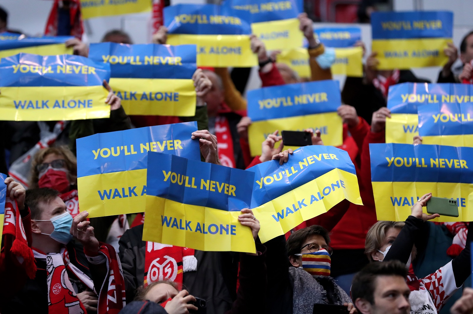 epa09829335 Fans show signs in Ukrainian colours reading 'You'll never walk alone' in support of Ukraine prior to the German Bundesliga soccer match between FSV Mainz 05 and Borussia Dortmund in Mainz, Germany, 16 March 2022.  EPA/FRIEDEMANN VOGEL CONDITIONS - ATTENTION: The DFL regulations prohibit any use of photographs as image sequences and/or quasi-video.