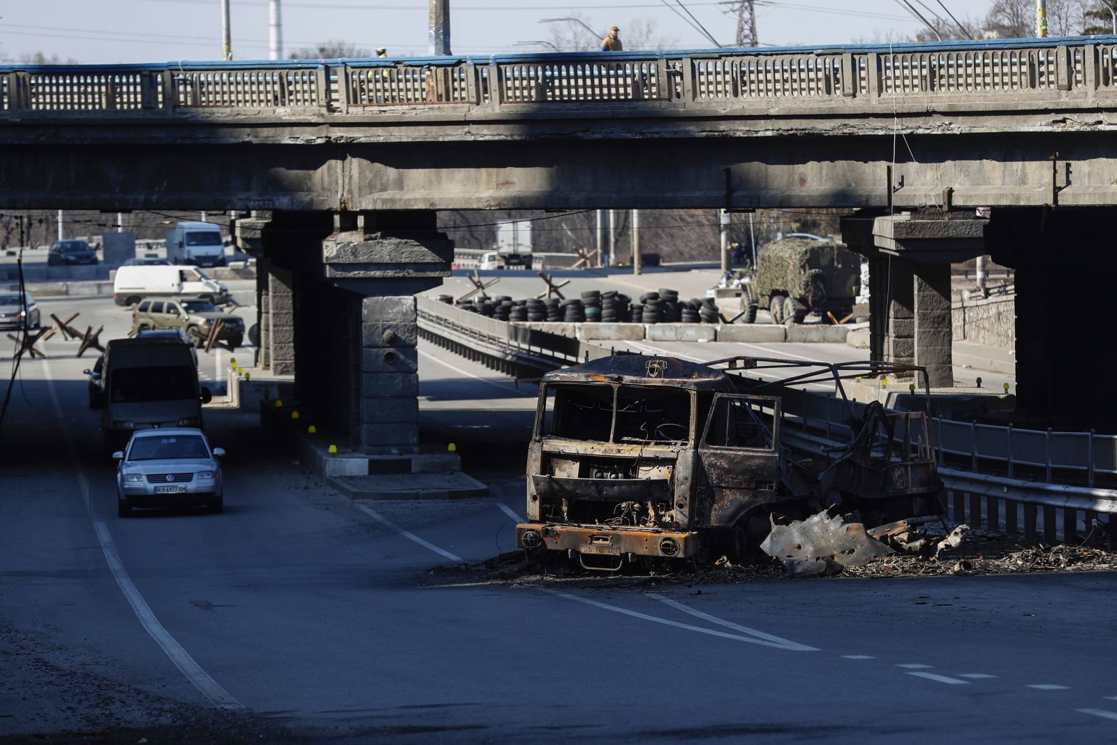 epa09836705 Ukrainian soldiers (top) stand guard on a bridge in front of a damaged Russian army car on the road that leads East of the Ukrainian capital of Kyiv, 19 March 2022. On 24 February Russian troops had entered Ukrainian territory in what the Russian president declared a 'special military operation', resulting in fighting and destruction in the country, a huge flow of refugees, and multiple sanctions against Russia.  EPA/ATEF SAFADI