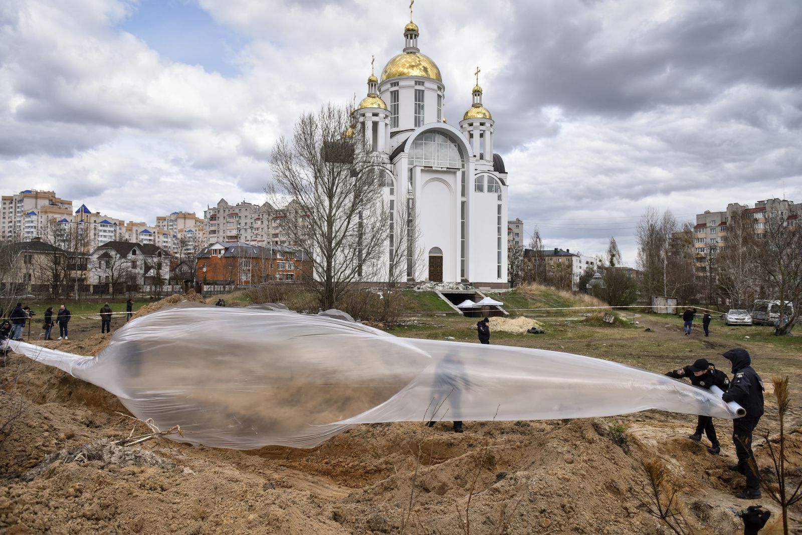 epaselect epa09885933 Police officers cover a mass grave with a plastic sheet as members of an international team of war crimes prosecutors and the Prosecutor General of Ukraine visit a mass grave in Bucha, Kyiv (Kiev) area, Ukraine, 12 April 2022. Forensic investigators began exhuming a mass grave in Bucha containing more than 410 bodies of civilians, according to Ukrainian officials. The UN Human Rights Council has decided to launch an investigation into the violations committed after Russia's full-scale invasion of Ukraine, the Ukrainian Parliament reported. Russian troops entered Ukraine on 24 February resulting in fighting and destruction in the country and triggering a series of severe economic sanctions on Russia by Western countries.  EPA/OLEG PETRASYUK