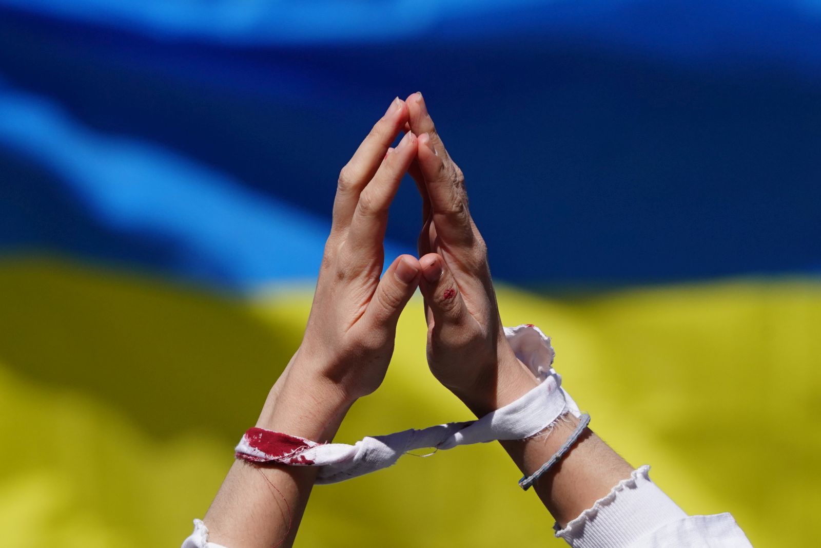 epa09892742 A participant of an Alternativer Ostermarsch (’Alternative Easter March') demonstrates with tied hands and artificial blood in front of a Ukrainian flag under the motto ’Stop Russian Wars’ in Berlin, Germany, 16 April 2022. This year’s peace and Easter marches are taking place under the impression of the ongoing war of Russia on Ukraine. A cooperation, among them Ukrainian, Syrian and Belarusian organizations, called for an alternative Easter march.  EPA/CLEMENS BILAN