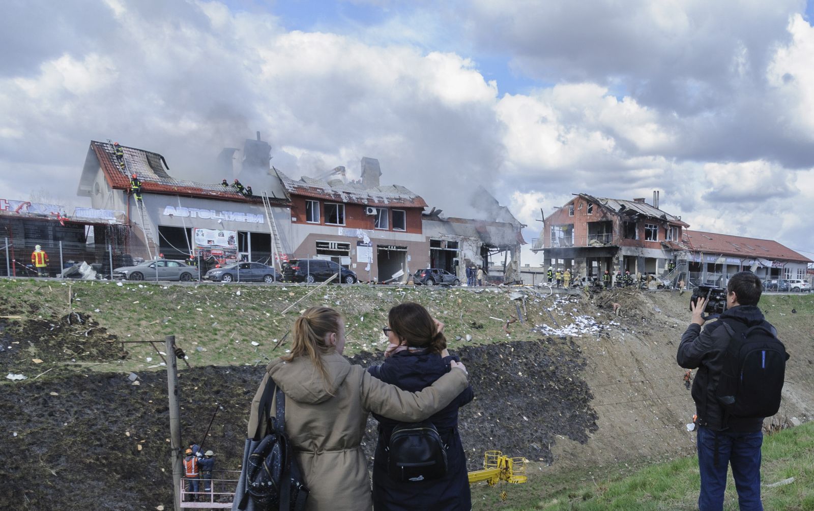 epaselect epa09895738 People look as Ukrainian rescuers put out a fire of an auto service center after Russian shelling in the western Ukrainian city of Lviv, Ukraine, 18 April 2022. According to Lviv authorities, seven civilians were killed and eleven people injured as Russian troops shelled Lviv's civilian infrastructure.  EPA/MYKOLA TYS