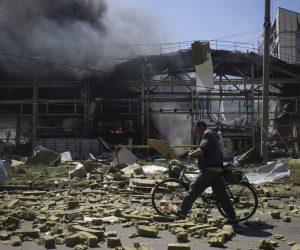 epa09980178 A local man pushing a bicycle walks past a building on fire after shelling in the small city of Bakhmut, Donetsk region, Ukraine, 27 May 2022. On 24 February, Russian troops invaded Ukrainian territory starting a conflict that has provoked destruction and a humanitarian crisis. According to the United Nations High Commissioner for Refugees (UNHCR), more than 6.6 million refugees have fled Ukraine, and a further 7.7 million people have been displaced internally within Ukraine since.  EPA/STRINGER