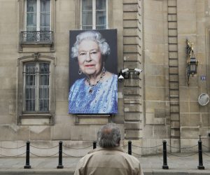 epa10172430 A person stands in front of a portrait of Britain's Queen Elizabeth II hanging outside the British embassy in Paris, France, 09 September 2022. Britain's Queen Elizabeth II died at her Scottish estate on 08 September 2022. The 96-year-old Queen was the longest-reigning monarch in British history.  EPA/TERESA SUAREZ