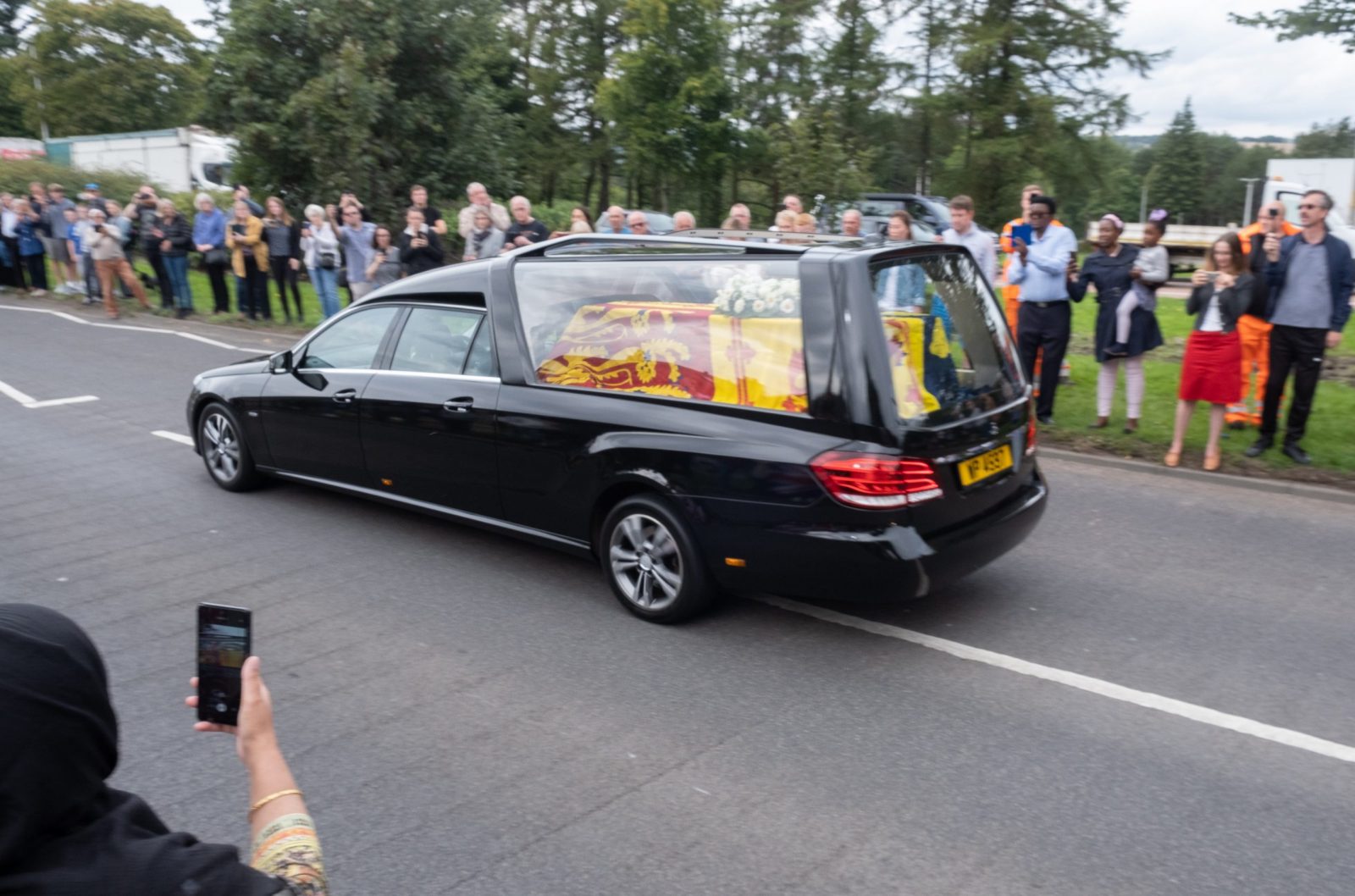 epa10177899 People stand to pay their respects as the hearse carrying the body of Queen Elizabeth II makes its way towards Edinburgh, in Dundee, Scotland, Britain, 11 September 2022. Britain's Queen Elizabeth II died at her Scottish estate on 08 September. The late queen will lie in state for 24 hours at St Giles' Cathedral in Edinburgh.  EPA/PAUL REID