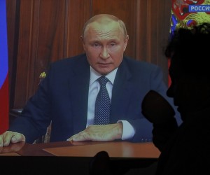 epa10196253 Lidia, a 75-year-old refugee from Mariupol, drinks morning tea as she is silhouetted against a TV screen displaying Russian President Vladimir Putin during a televised address to the nation, in Moscow, Russia, 21 September 2022. President Putin has signed a decree on partial mobilization in the Russian Federation, with mobilization activities starting on 21 September. Russian citizens who are in the reserve will be called up for military service.  EPA/SERGEI ILNITSKY