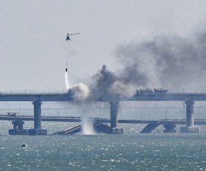 epaselect epa10230640 A firefighter helicopter pours water on fire on a collapsed part of the Kerch Strait bridge in Crimea, 08 October 2022. According to Russian authorities, "an explosion was set off at a cargo vehicle on the motorway part of the Crimean bridge on the side of the Taman peninsula, which set fire to seven fuel tanks of a train that was en route to the Crimean peninsula. Two motorway sections of the bridge partially collapsed."  EPA/STRINGER